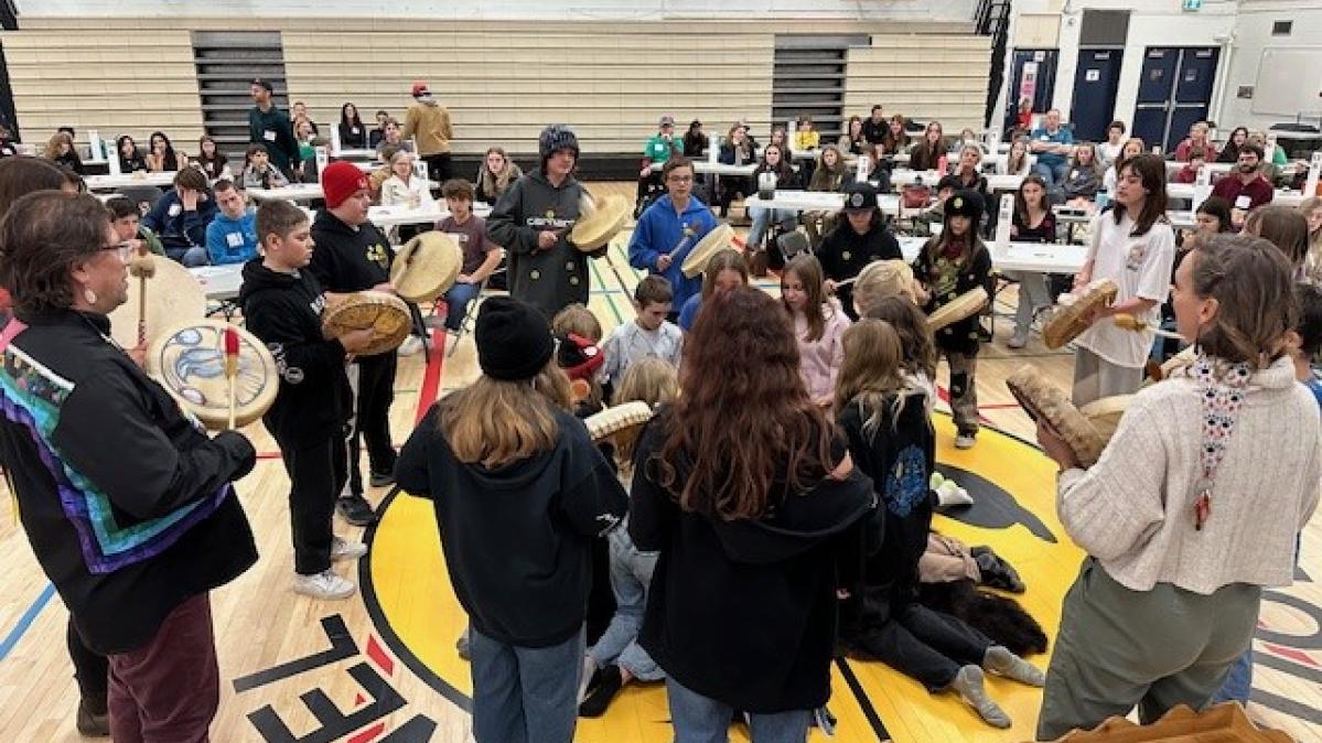 Staff and students drumming in a circle in a school gymnasium.