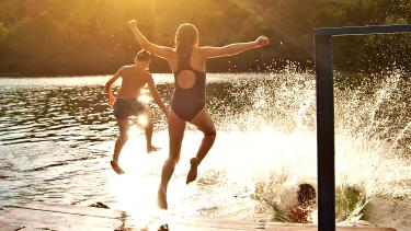 Three children in their bathing suits jumping into a lake from a dock at sunset.