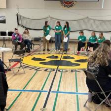 Students seated and standing at the centre of a school gymnasium.