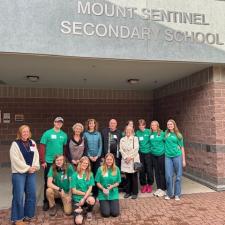 Youth and adults posing as as group in front of a school gymnasium.